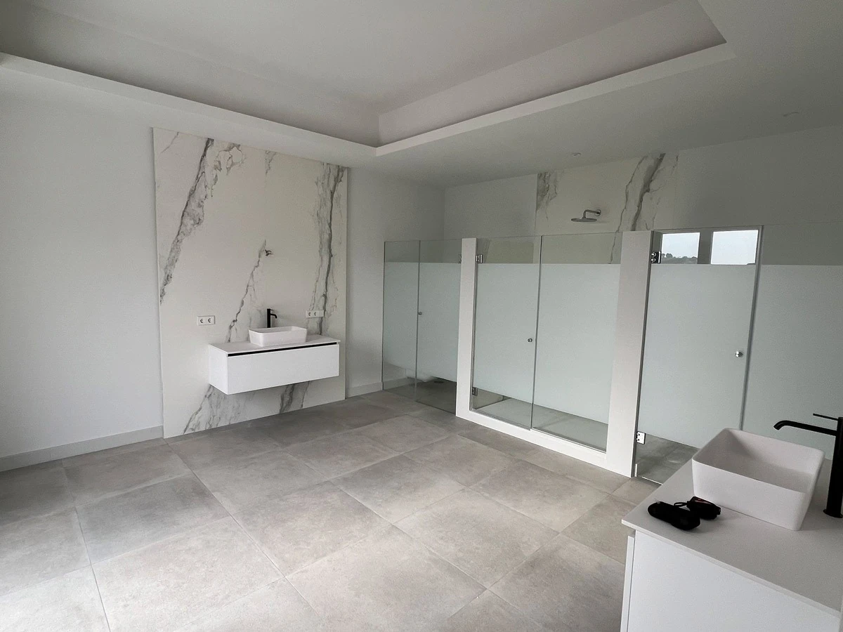 Bathroom before redesign, with white vanity units and a glass shower