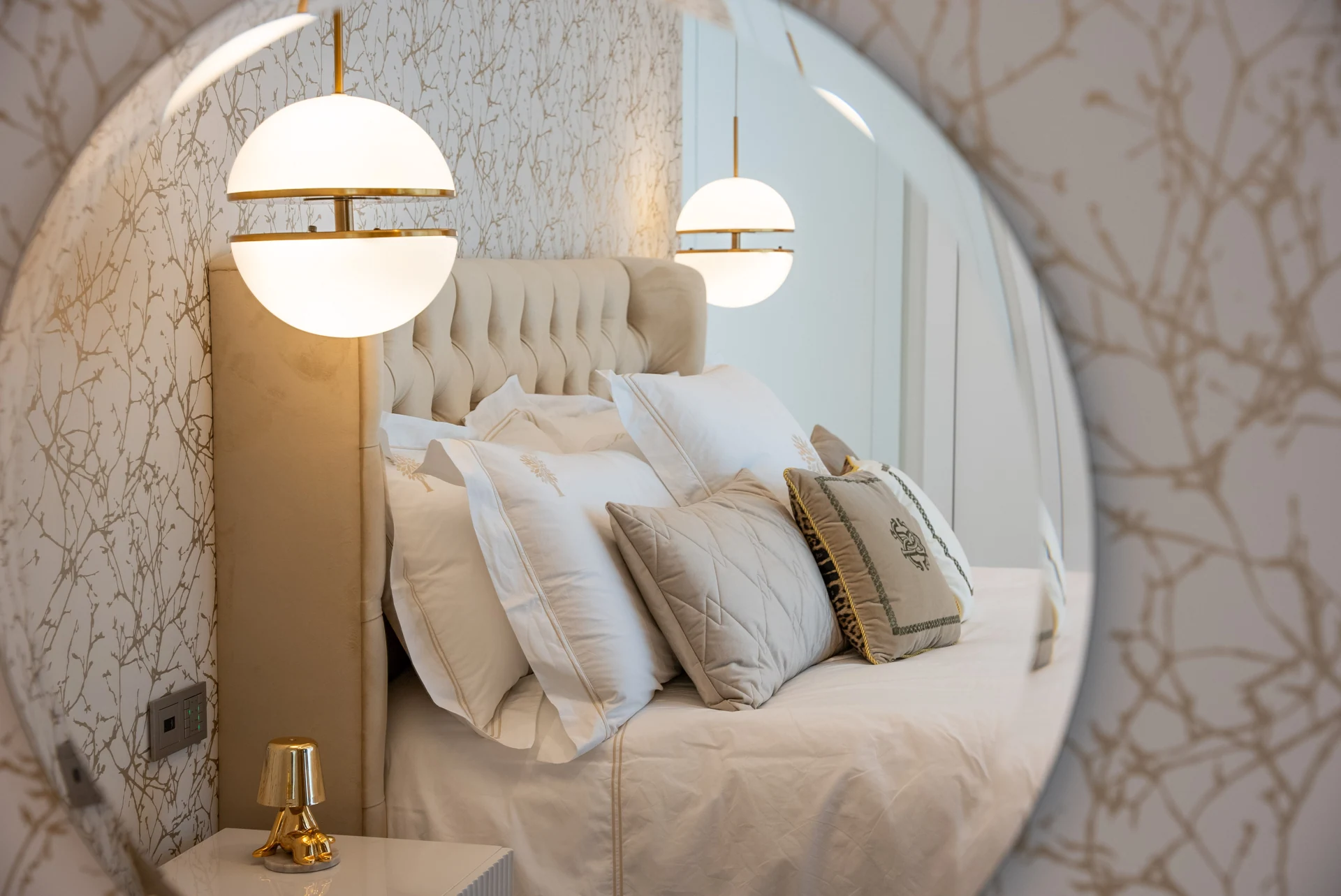 Round mirror reflecting an upholstered bed