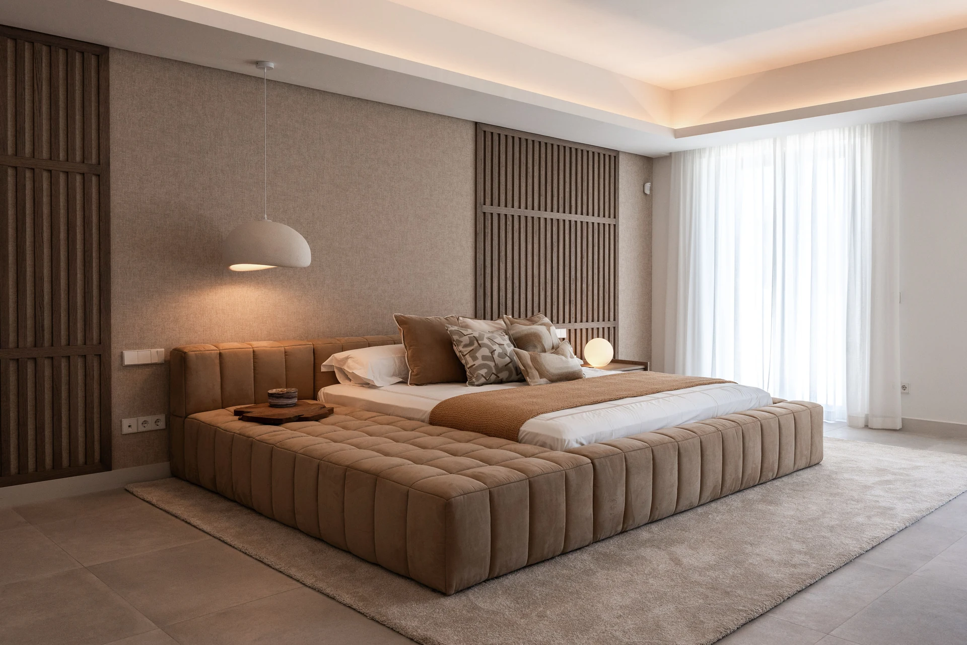 Finished bedroom with an upholstered bed, timber wall detailing, textured finishes and soft curtains