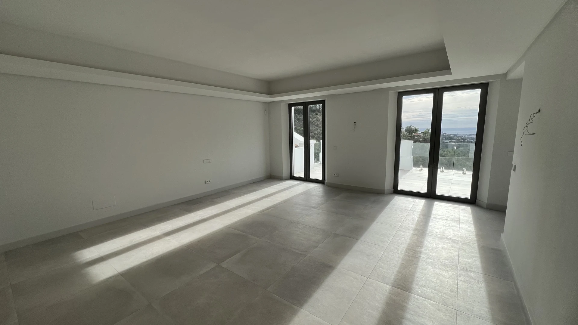 Empty bedroom before furnishing, with plain walls and glazed doors opening to a terrace